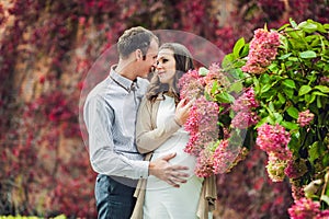 A pregnant young woman and her husband. A happy family standing at the red autumn hedge, smelling a flower hydrangea. pregnant