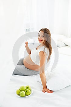 Pregnant Young Woman holding Apple while sitting on the Bed. Hea