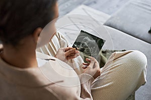 Pregnant young woman holding ultrasound picture of baby enjoying motherhood