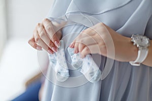 Pregnant Young Woman Holds Shoes for Newborn. Happy Motherhood Concept. Healthy Pregnancy Concept. Young Mother. Little Shoes on