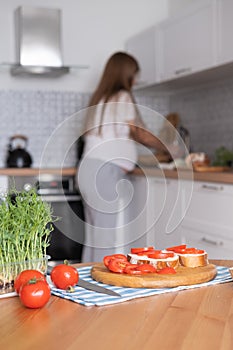 Pregnant young woman preparing healthy sandwiches with microgreens and vegetables at home in the kitchen