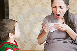 Pregnant young woman scared with nosebleed. A little boy looks at his pregnant mom. Healthcare and medical concept photo