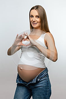 Pregnant young woman showing heart sign and smiling nicely