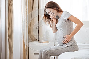 Pregnant young woman sitting on bed and feeling sick photo