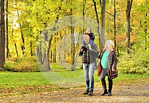 Pregnant young woman walking in autumn park with her husband and child
