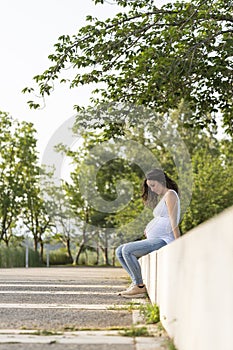 Young pregnant woman looking her belly sitting in the street