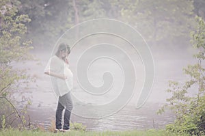 Pregnant woman by foggy river