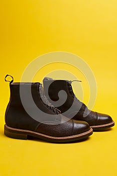 Premium Dark Brown Grain Brogue Derby Boots Made of Calf Leather with Rubber Sole Placed Over One Another On Yellow