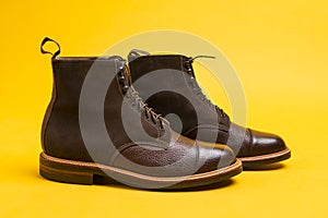Premium Dark Brown Grain Brogue Derby Boots Made of Calf Leather with Rubber Sole Placed Over One Another On Yellow Background