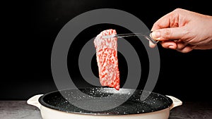 Premium Rare Slices sirloin Wagyu A5 beef with high-marbling texture pick up over marble coated non-stick pan by bbq tongs.