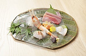 Premium Sashimi garnished with edible flowers in green ceramic plate on wooden background