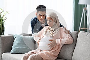 Prenatal Contractions. Caring husband comforting his pregnant muslim wife suffering abdominal pain