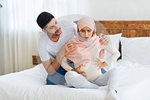 Prenatal contractions. Pregnant muslim woman suffering from abdominal pain and caring arab husband comforting wife