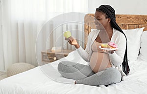 Prenatal Nutrition. Black Pregnant Woman Choosing Between Apple And Donuts At Home