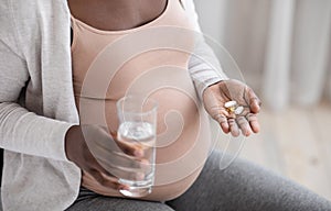 Prenatal Vitamins And Supplements. Unrecognizable black pregnant woman taking pills and water