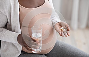 Prenatal Vitamins And Supplements. Unrecognizable black pregnant woman taking pills and water photo