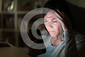 Preoccupied adult woman reading on phone at night at home photo