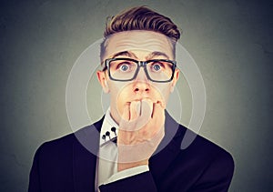 Preoccupied anxious young business man in glasses biting his fingernails looking at camera photo