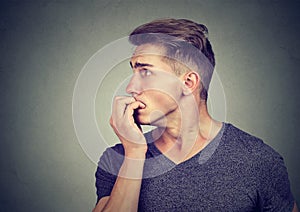 Preoccupied anxious young man biting his fingernails looking to the side