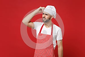 Preoccupied male chef cook or baker man in striped apron white t-shirt toque chefs hat posing isolated on red background