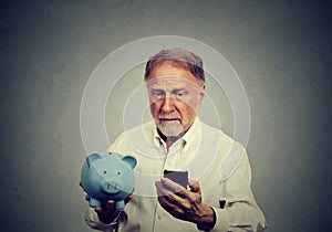 Preoccupied man looking at his mobile phone holding piggy bank photo