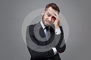 Preoccupied tired young bearded business man in classic black suit shirt tie posing isolated on grey background photo