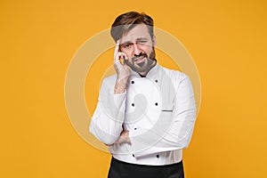 Preoccupied tired young bearded male chef cook or baker man in white uniform shirt posing isolated on yellow background