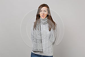 Preoccupied young woman in gray sweater, scarf holding hands behind her back isolated on grey background. Healthy
