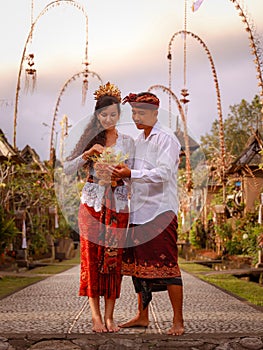 Preparation for Balinese ceremony. Multicultural couple preparing for Hindu religious ceremony with god`s offerings. Penjor bambo