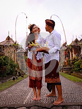 Preparation for Balinese ceremony. Multicultural couple preparing for Hindu religious ceremony with god`s offerings. Penjor bambo