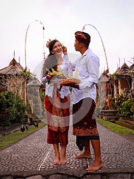 Preparation for Balinese ceremony. Multicultural couple preparing for Hindu religious ceremony with god`s offerings. Penjor bambo