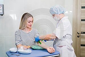 Preparation for blood test with beautiful young blond woman by female doctor in white coat medical uniform on the table