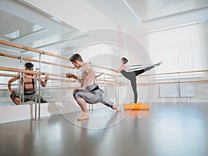 Preparation of body before performance in ballet studio. Male dancer and ballerina warming up near barre on rehearsal