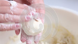 Preparation of cheese cakes. A woman rolls and forms a dough. In the container is cottage cheese and a chicken egg is knocked out.