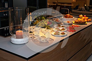 Preparation for Christmas banquet. Wine glasses, snacks on the modern kitchen table are ready to serve. Evening lights