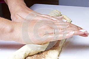 Preparation of cinnamon rolls. The woman turns off the dough with a filling of cinnamon and sugar.