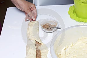 Preparation of cinnamon rolls. The woman turns off the dough with a filling of cinnamon and sugar.