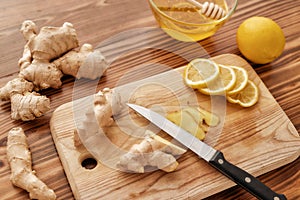 Preparation of cold and flu remedy cure drink, Close up of board, knife, fresh ginger, lemon, honey in a bowl with