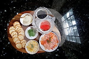 Preparation of delicious but expensive red and black caviar with crackers, smoked salmon, dill, lemon and cream