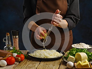 Preparation of dishes with grated cheese - pasta, pizza, risotto, salad. Chef rubs cheese on a manual grater on a dark blue