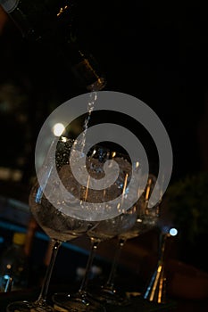 Preparation of drinks with ice in three glass glasses, bar in the evening in the background.