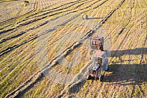 Preparation of feed for livestock. An old tractor picks up and presses hay into rolls. Shooting from a drone