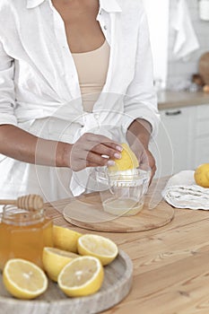Preparation of fresh llemonade. Young girl squeezes lemon juice in the kitchen near the window