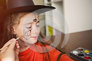 Preparation for Halloween. child in a witch outfit doing face painting. cute spider. idea of simple suit, diy