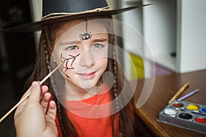 Preparation for Halloween. child in a witch outfit doing face painting. cute spider. idea of simple suit, diy