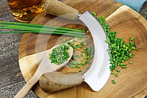 Preparation of herbs for meal:  brown wood cutting board with chefÃÂ´s mincing knife, chopped green chives and wooden spoon