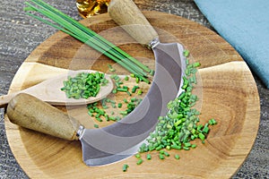 Preparation of herbs for meal:  brown wood cutting board with chefÃÂ´s mincing knife, chopped green chives and wooden spoon