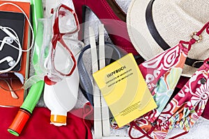 Preparation for holiday, luggage with swimwear, towel, sunglasses, suncream, flip flops, straw hat, vaccination pass