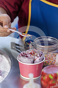 The preparation of ice-cream , Thai street food, cook sprinkles ice cream in a paper Cup with caramel. Vertival photo