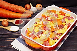 Preparation for meat casserole with vegetables. Sliced â€‹â€‹meat, onions, carrots and potatoes in orange deco for baking.